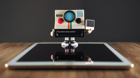 A Polaroid Funki Pop! standing on top of an iPad Air 2 on a wooden surface