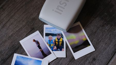 The Fujifilm Instax Mini Link 3 mobile photo printer on a gray background with instant photos